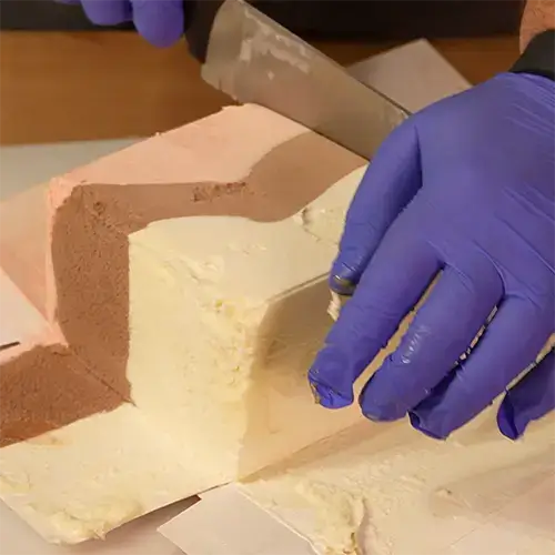 A person wearing blue nitrile gloves using a knife to cut a frozen block of Neapolitan ice cream.