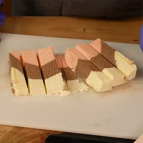 6 long pieces of frozen Neapolitan ice cream on a cutting board.