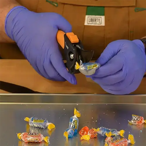 A man with nitrile gloves cutting jolly ranchers using a pair of clean garden pruners.