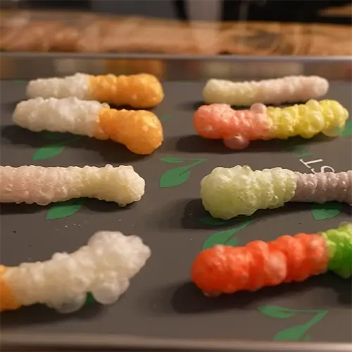 8 freeze dried mini gummy worms that have puffed up much larger than their original size.