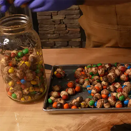 A mason jar and a Harvest Right tray with freeze dried Caramel M&M's with a man wearing blue nitrile gloves moving the M&M's from the tray to the jar.