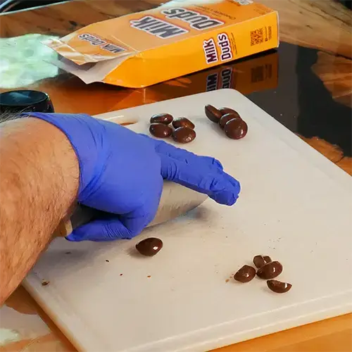 A man waring blue nitrile gloves using a kitchen knife to cut a Milk Dud in half. 