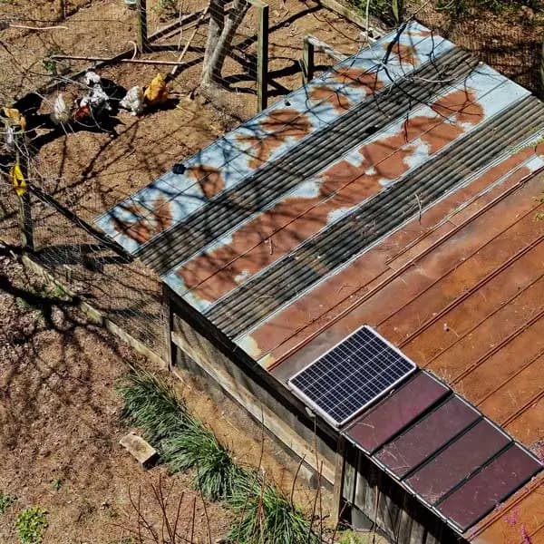 Aerial view of a rustic chicken coop with a corrugated metal roof, featuring a small solar panel.