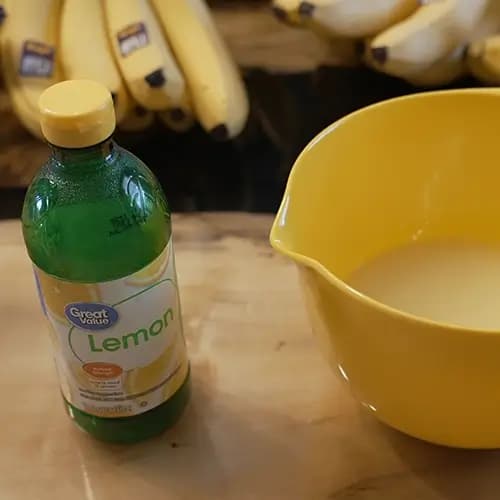 A container of lemon juice sitting next to a yellow mixing bowl with some bananas in the background.