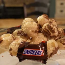 An array of puffed up freeze dried Snickers behind a Snickers Mini wrapper. 