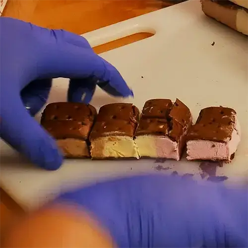 A frozen Neapolitan ice cream sandwich cut into eighths on a cutting board.