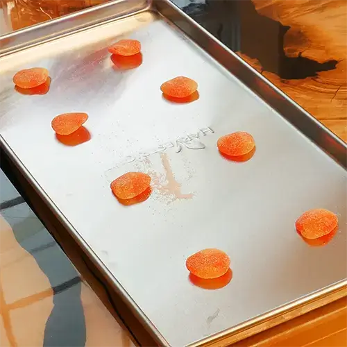 A diagonal view of eight Haribo Peaches placed neatly in rows on a medium Harvest Right freeze dry tray.