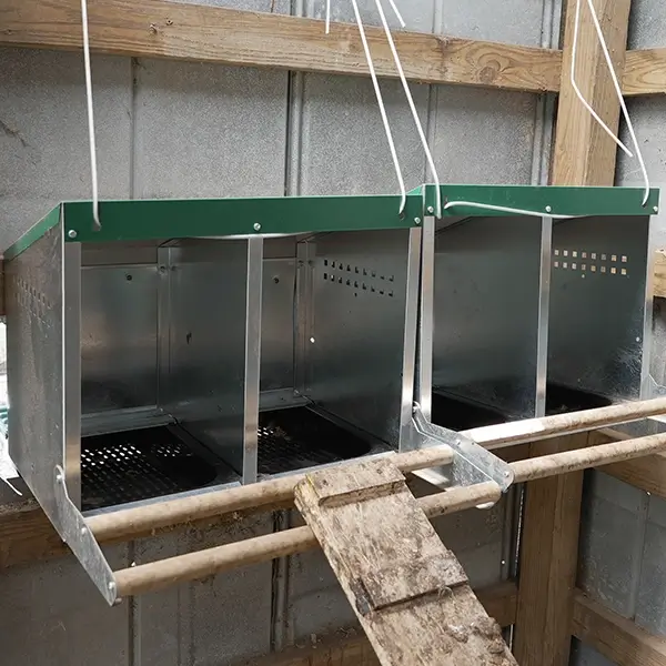 A silver and green roll away nesting box strapped up to a wall using wire. 