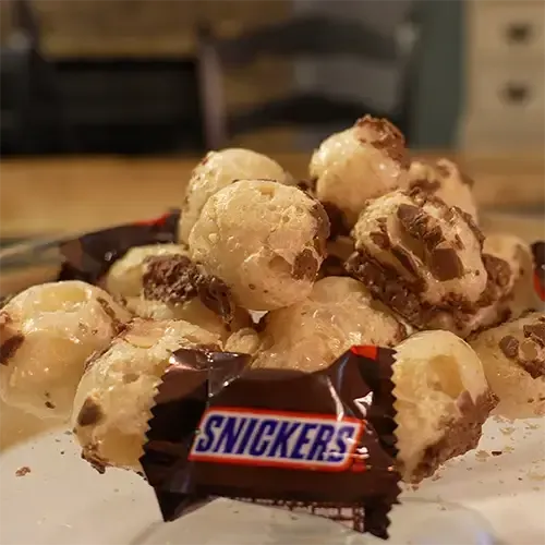 An array of puffed up freeze dried Snickers behind a Snickers Mini wrapper. 